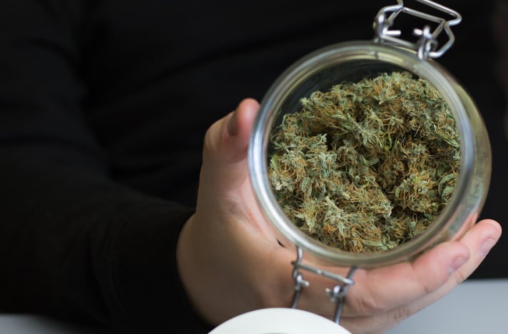 A top-down view of a hand holding an open jar of cannabis.